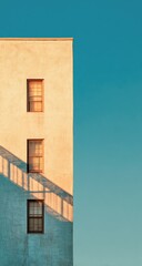 A pale beige building, sunlit, casts a soft shadow against a vibrant teal sky