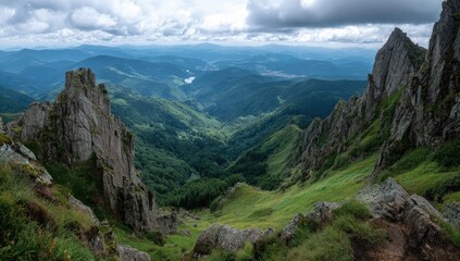 Obraz premium Dramatic mountain vista. A valley with lush green slopes, deeply cut by a narrow gorge, is framed by jagged, gray-rock peaks. A high elevation viewpoint