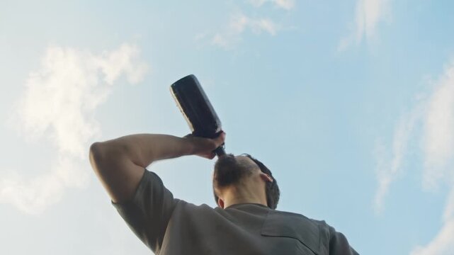An alcoholic man who is intoxicated takes a sip of wine from a bottle, but later he feels sick and vomits on camera. Low angle. Slow motion.
