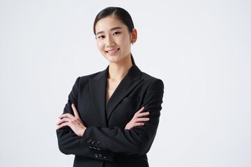 A smiling woman in a smart business suit, with crossed arms, confidently looks directly at the camera. The image captures professional and confident demeanor