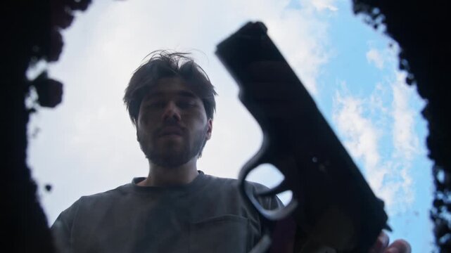 Male offender excavates pit in earth and conceals firearm within it. He is concealing evidence of criminal act he has perpetrated. Low angle.