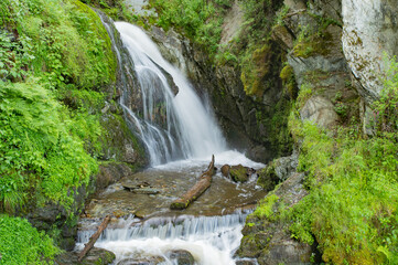 A small picturesque waterfall among mountain slopes covered with bright greenery