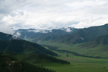 Mountain valley with lush green grass surrounded by mountain ranges covered with clouds