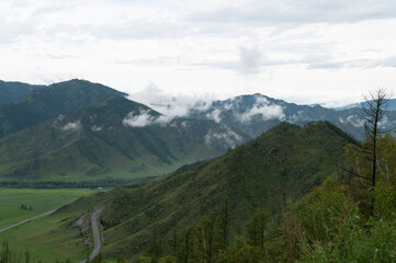 Mountain valley with lush green grass surrounded by mountain ranges covered with clouds