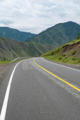 An asphalt road in a mountainous area stretching into the distance between the slopes of high hills.