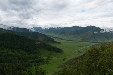 Mountain valley with lush green grass surrounded by mountain ranges covered with clouds