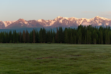 The mountain tops are covered with snow and illuminated by the reddish morning light.