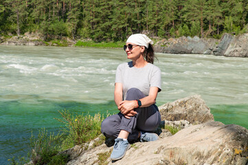 An adult attractive woman sits on the rocks on the bank of a mountain river