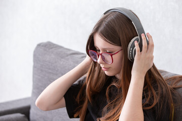 Young girl enjoying music with headphones while sitting on a couch in a modern living room during daytime