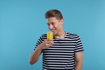 Fototapeta premium Happy man with glass of orange juice on light blue background. Refreshing drink