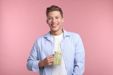 Happy man with mason jar of lemonade on pink background. Refreshing drink