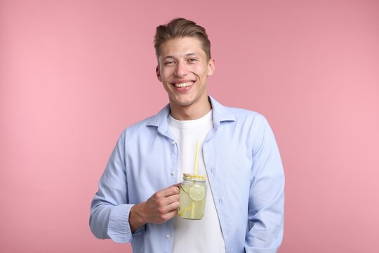 Happy man with mason jar of lemonade on pink background. Refreshing drink