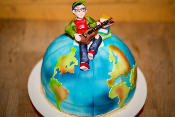 Detailed view of the globe-shaped cake with fondant figurine of a boy playing guitar, sitting on...