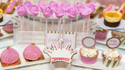 Candy bar setup with pink crown-shaped cookies, cupcakes topped with cream, and lollipop bouquets, perfect for a princess-themed birthday party.