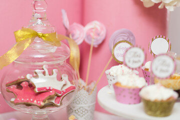 Close-up of a glass jar with crown cookies and cupcakes decorated with cream, creating a sweet and festive candy bar display.