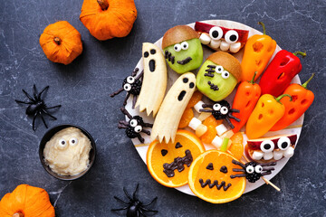 Healthy Halloween fruit and vegetable platter. Assortment of fun, spooky treats. Top down view table scene over a white marble background.