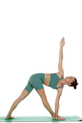 Studio shot of young woman in green outfit doing triangle yoga pose (trikonasana) on white background.