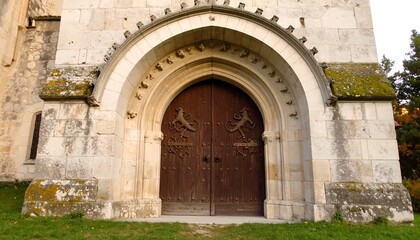 Fototapeta premium Ancient Stone Church Entrance with Large Wooden Double Doors and Arched Facade.