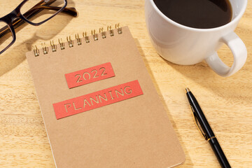 New year 2022 planning concept. Notepad, cup of coffee and eyeglasses on wooden desk