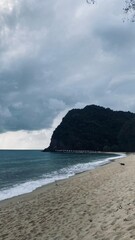 A scenic beach with a mountain in the background under a cloudy sky.
