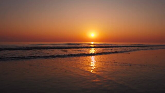 Low angle shot of of small waves crashing on shore during sunset at Mandvi, Kutch, India. Beautiful beach with orange setting sun. Summer vacation background. Travel and holidays concept.