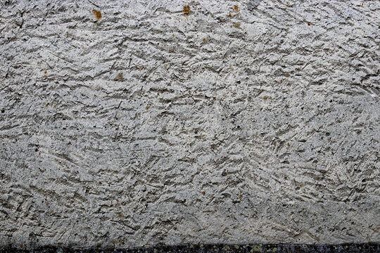 Gray textured surface. Grainy texture with uneven coloring, which may be caused by lighting or typical material. Imitation of liquid wallpaper.