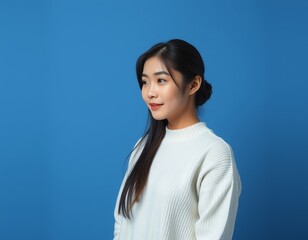 Portrait of a young asian woman with long dark hair and white sweater on blue background