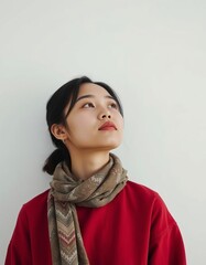 Portrait of a young woman with a scarf looking up against a white background wall