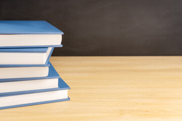 Pile of books on wooden table and black chalkboard at background with copy space. Back to school, education or learning concept