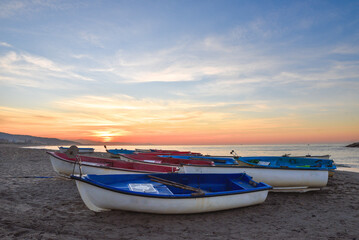 Naklejka premium small wooden Fishing row boat on sandy beach in Mediterranean sea, White fishing boats by the sea, Boat on the beach at sunset time, A Small Boat Moored on a Beach. coastline, In Jijel Algeria Africa.
