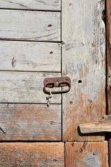 A close-up photograph of an old, weathered wooden door with a rusty metal handle and peeling paint