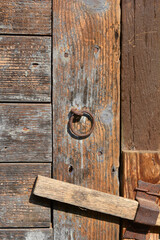 Fototapeta premium A close-up shot of an old wooden door featuring a weathered metal ring and a wooden latch, showcasing texture and patina