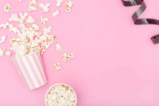 Popcorn bucket and film strip on pink background. Movie or TV background. Top view Copy space