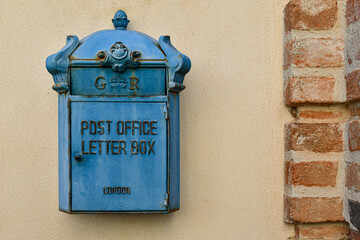 A classic British-style vintage blue letterbox mounted on a light yellow and brick wall, Italy
