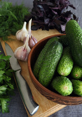 Cucumbers in a wooden bowl and greens on a cutting board.