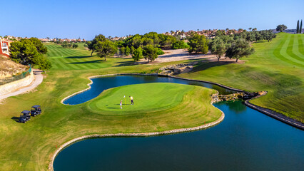 Golfers playing on beautiful green surrounded by water in golf course