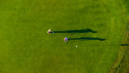Golfers playing on green grass golf course on sunny day, aerial view