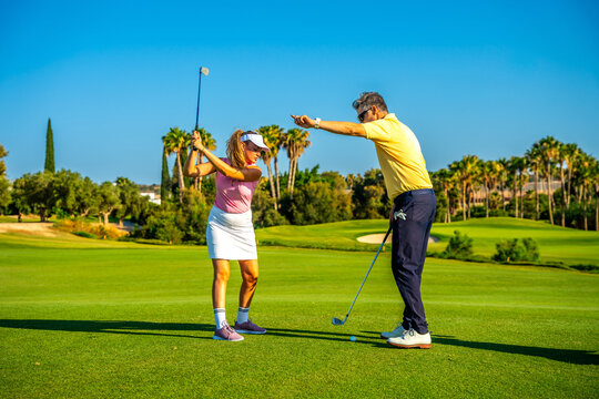 Golf instructor coaching female golfer on driving range, improving her swing technique