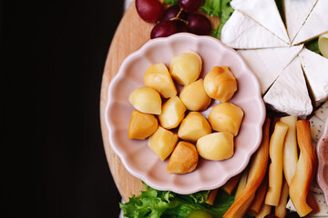 Cheese balls in pink bowl. Wooden board with brie cheese. Grapes and smoked sticks. Fresh lettuce leaves. Rustic snack background. Appetizer composition for wine. Tasty dairy products.