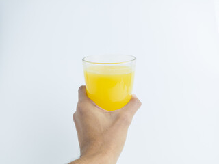 Hand holding a tall glass of fresh orange juice on white background. Isolated citrus drink concept, refreshing healthy beverage with minimalist style and copy space.
