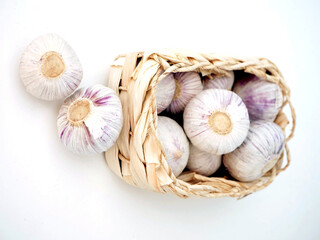 The image shows several heads of garlic spilling out of a small woven basket. Two garlic bulbs are also lying outside the basket.