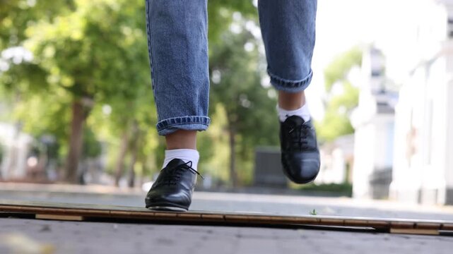 Teenage girl in tap shoes dancing outdoors, closeup. Camera moving left