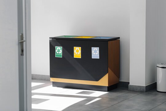 Indoor recycling bins with colored labels. Waste separation station in modern building hallway. Clean environment with sunlight on floor. Eco friendly container for garbage sorting. Sustainable waste.