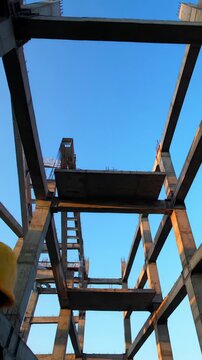 A cinematic, slow vertical pan video of an unclad modern high-rise building's steel & concrete framework, with a professional construction worker, bathed in golden hour light, emphasizing geometric