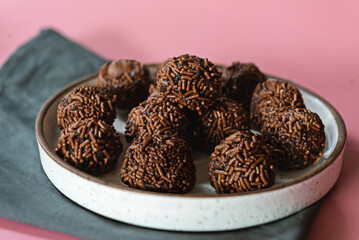 Brigadeiros com granulado no prato de cerâmica no fundo rosa 
