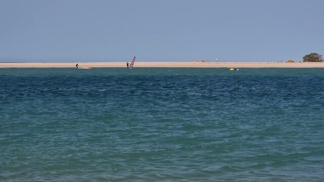 Surfers ride waves on Sancti Petri beach with scenic views of Sancti Petri Castle in Chiclana de la Frontera, C&aacute;diz, Spain. Coastal landscape ideal for themes of sport, travel, and heritage.