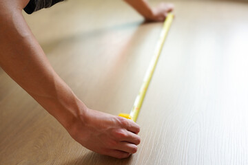 フローリングの床をメジャーで測定している男性　引越し、リフォームのイメージ