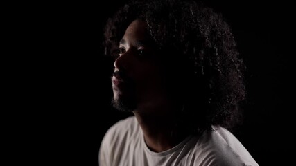 Portrait of a young African-American man with curly hair looking up, hoping, thinking, dreaming on black background - Powered by Adobe