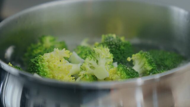 Fresh broccoli is submerged in boiling water, steaming gently as it cooks to become tender and vibrant