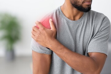 A close-up shot of a man holding his shoulder which is highlighted in red to indicate pain or inflammation.